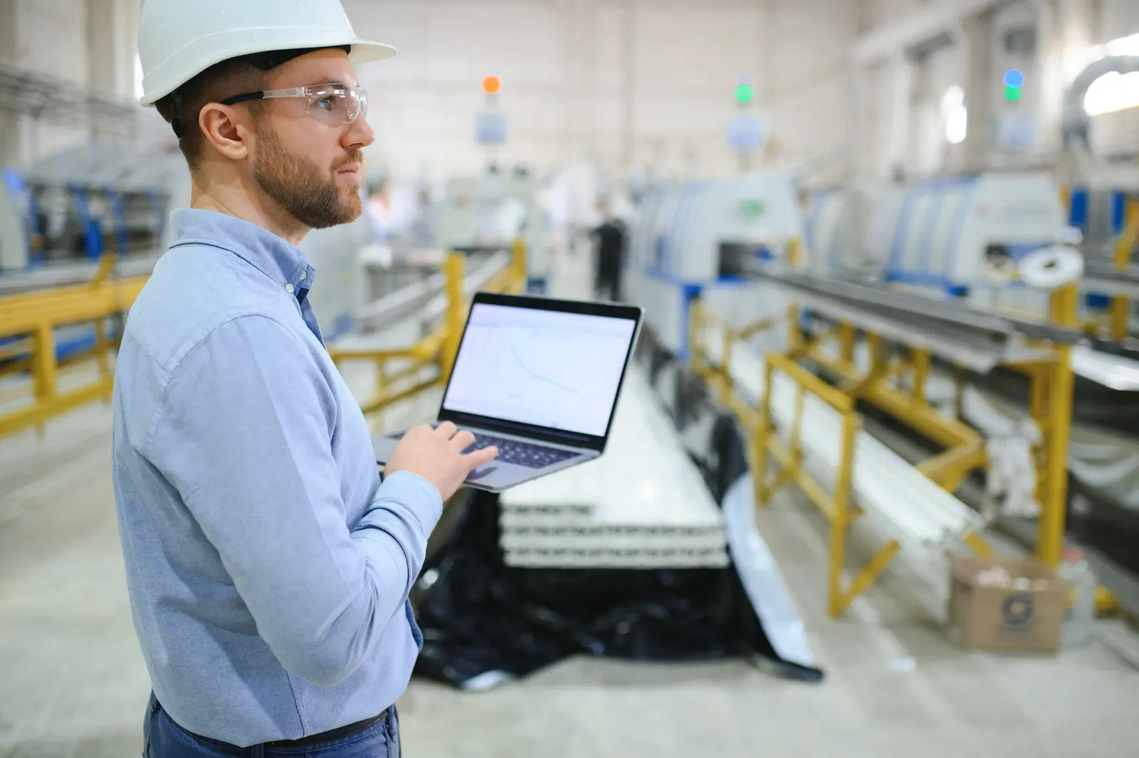 Ingeniero revisando datos en una notebook junto a una línea de producción industrial