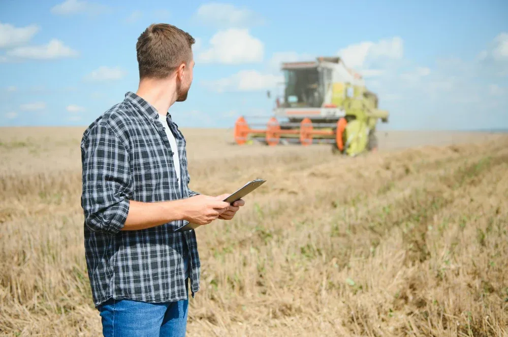 Encargado agroindustrial consultando una tablet en el campo junto a una cosechadora