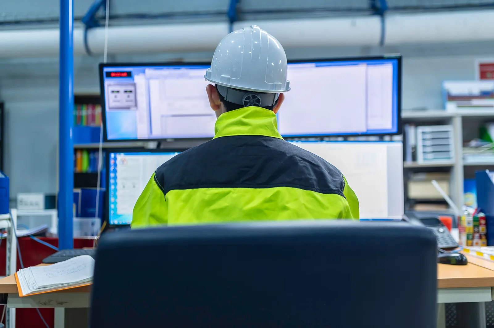 Ingeniera revisando tableros de datos de producción en varios monitores dentro de una planta industrial