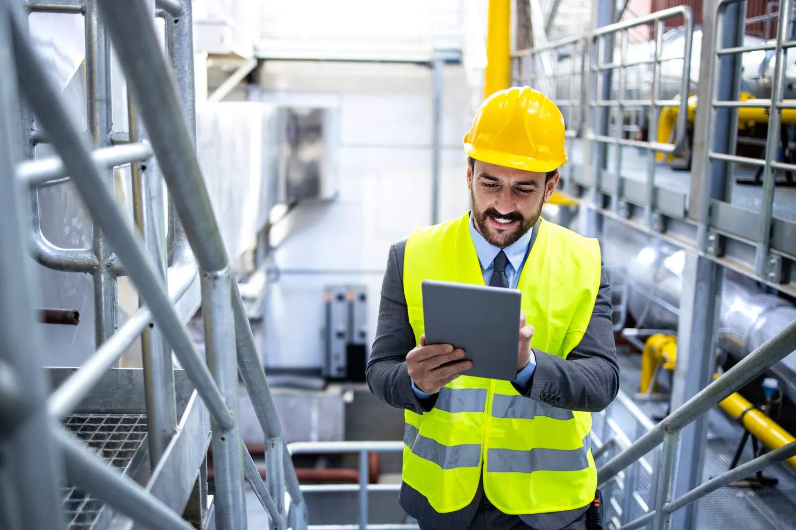 Responsable de planta con casco y chaleco reflectivo consultando una tablet en una pasarela de la sala de máquinas