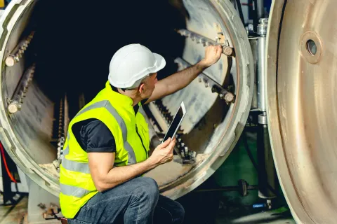 Técnico de mantenimiento registrando en una tablet los datos de una intervención sobre una caldera industrial